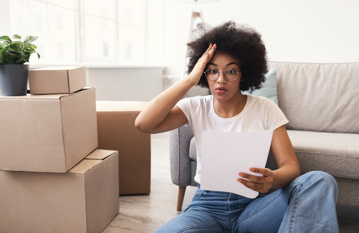 Woman Reading Sale Agreement Sitting Among Moving Boxes Indoors